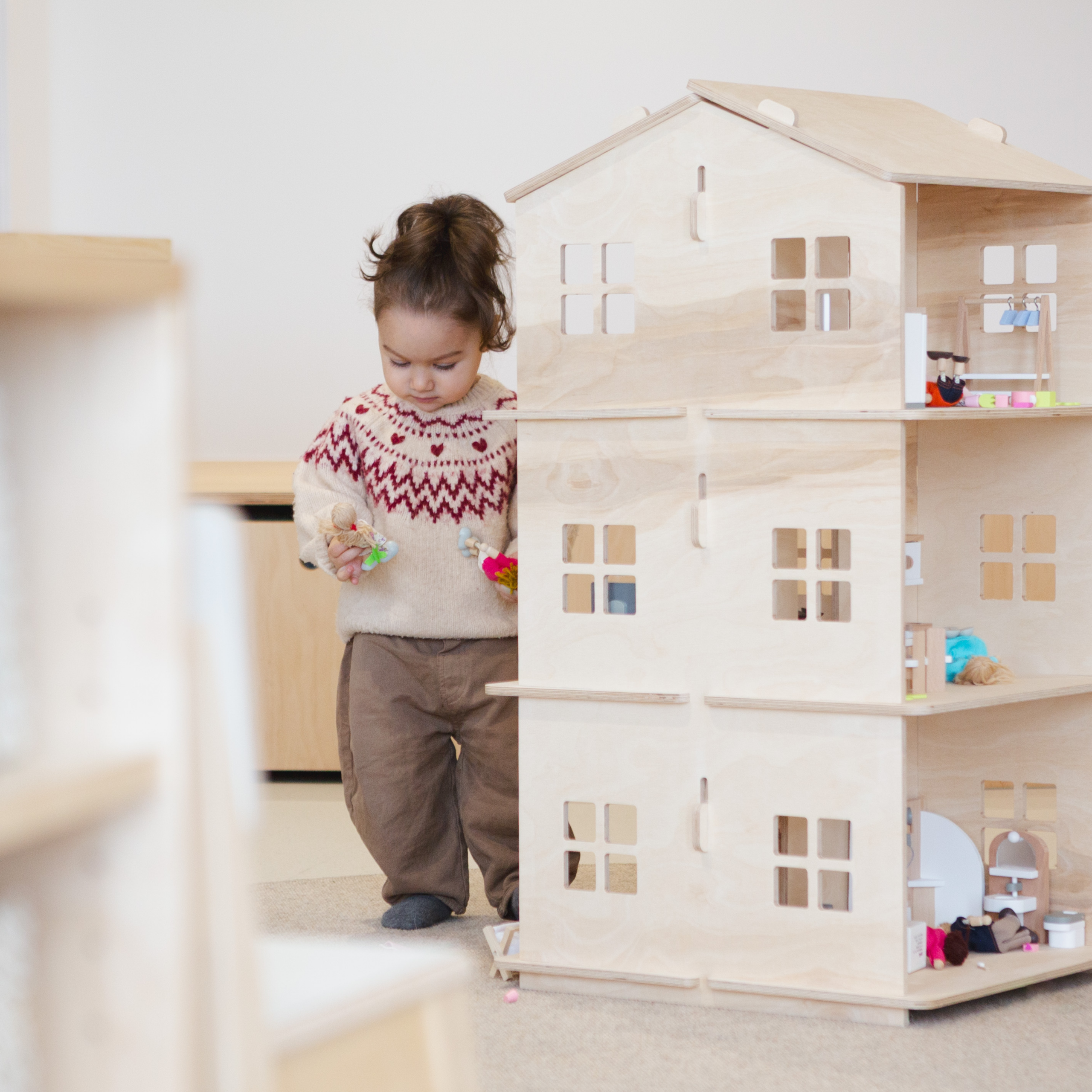 Ein Kinde, das mit einem großem Puppenhaus aus Holz spielt