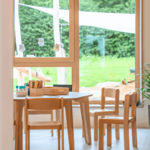 Stuhle im Vordergrund. Im Hintergrund sieht man durch das Fenster eine grüne Wiese.