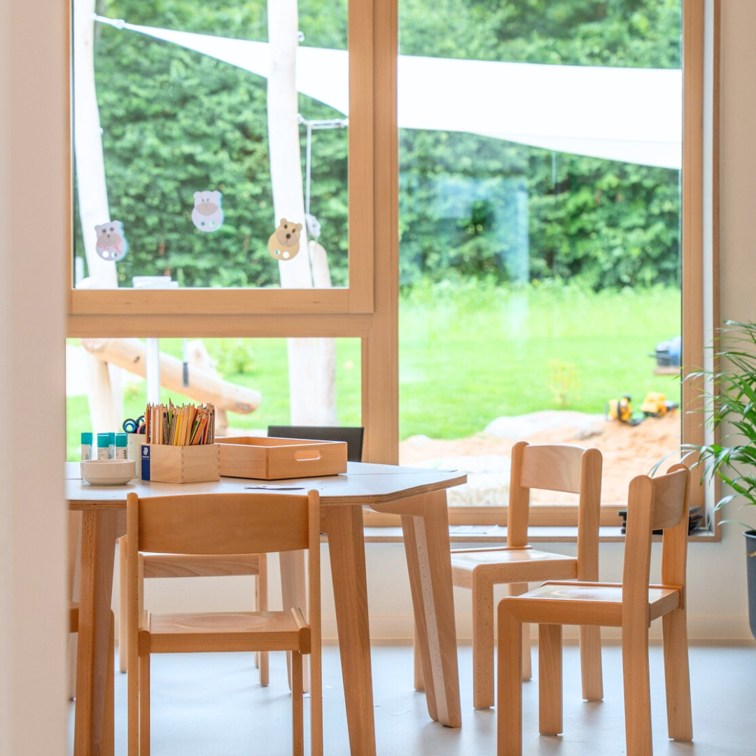 Stuhle im Vordergrund. Im Hintergrund sieht man durch das Fenster eine grüne Wiese.