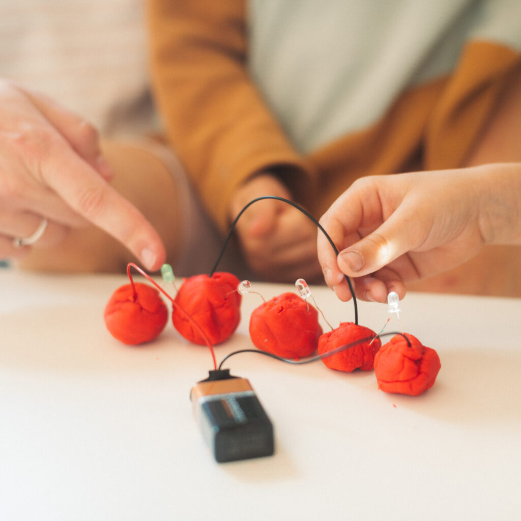 Kinder verbinden Knete mit Drähten um eine LED zum leuchten zu bringen