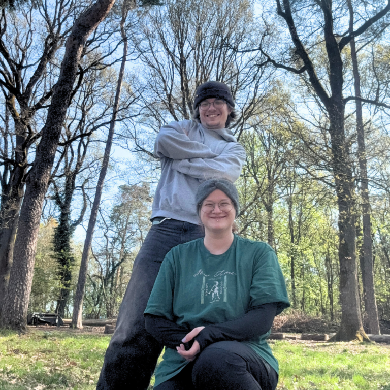 Ein Mann (Max) und eine Frau (Hannah) stehen und posieren im Wald.