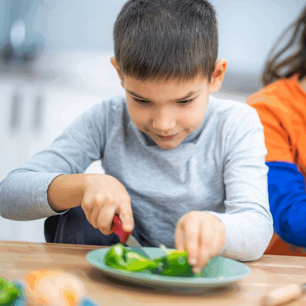 Kind schneidet Gemüse auf einem Teller.
