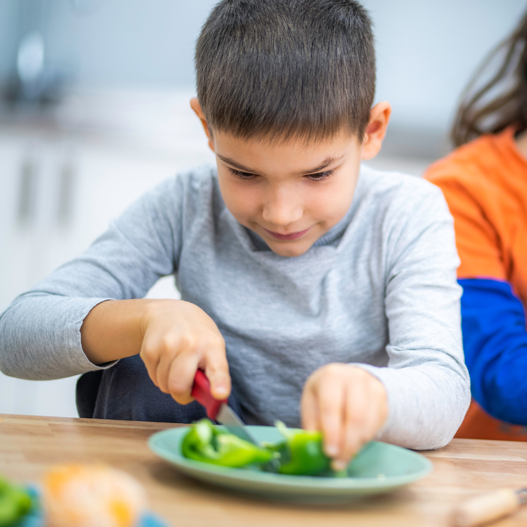 Kind schneidet Gemüse auf einem Teller.