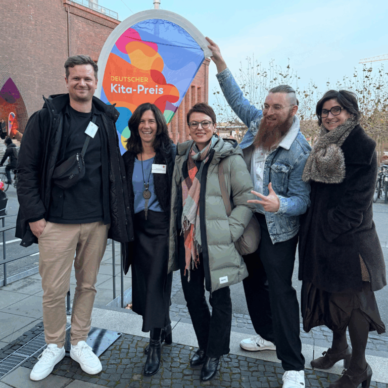 6 Personen stehen vor der bunten Kitapreis-Wand und halten einen großen Scheck in den Händen