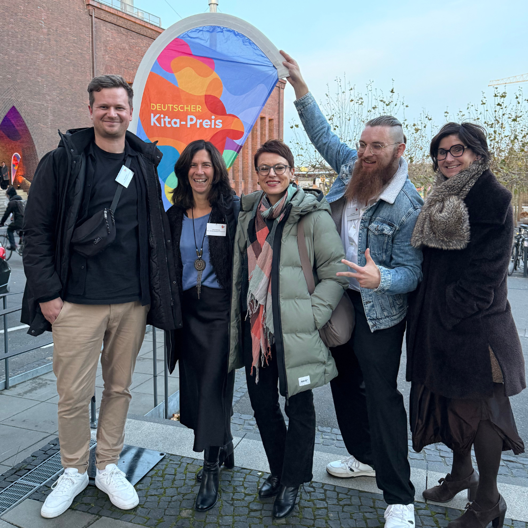 6 Personen stehen vor der bunten Kitapreis-Wand und halten einen großen Scheck in den Händen