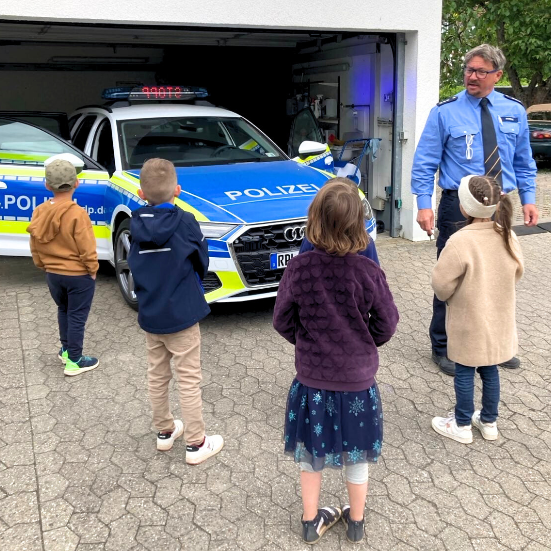 Verkehrserzieher steht mit Kindergartenkindern vor einem Polizeiauto.