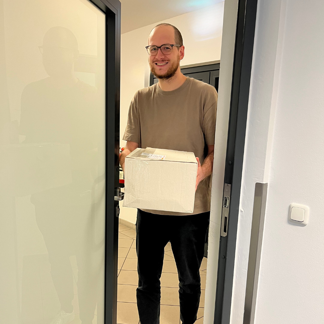 Ein Mann trägt ein Paket zur Tür hinein und freut sich.