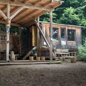 Holzhütte mit großem überdachtem Unterstand in einem Waldkindergarten, ausgestattet mit Werkbank, Sitzmöglichkeiten und Holzlager