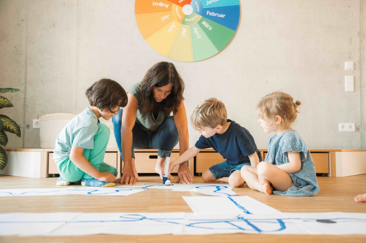 Frau malt zusammen mit Kindern eine Linie auf den Boden, auf der ein ozobot fährt